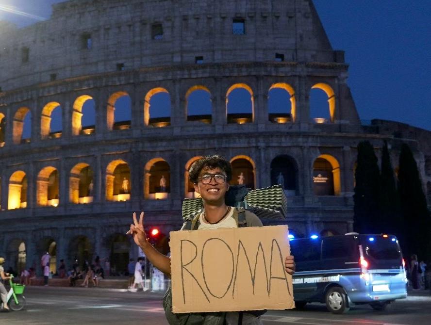 Yuheng Li in front of the Colosseum in Rome, holding a hitchhiking sign